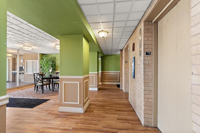 hall with light wood-type flooring, brick wall, and elevator