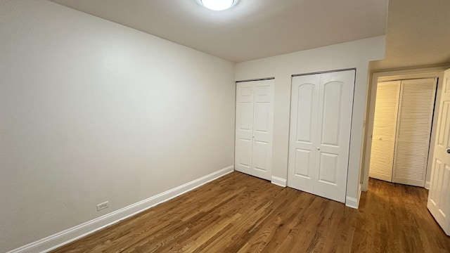 unfurnished bedroom with dark wood-type flooring and two closets