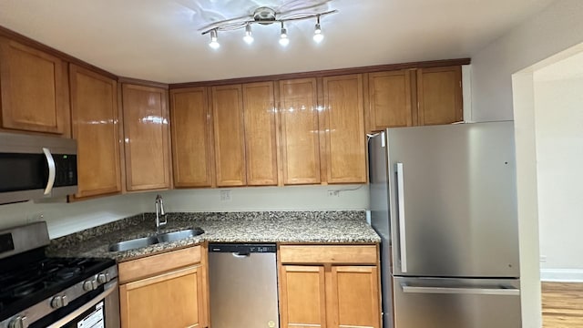 kitchen featuring stainless steel appliances, light hardwood / wood-style floors, dark stone counters, and sink