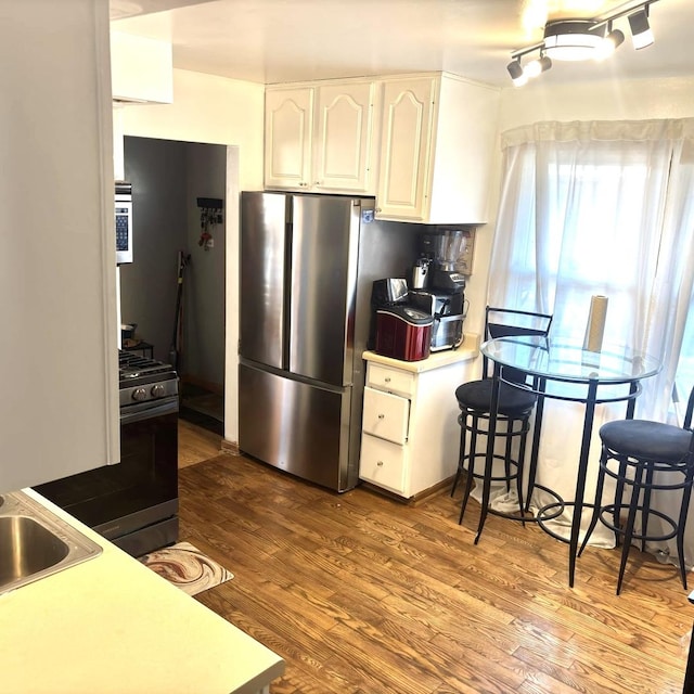 kitchen with appliances with stainless steel finishes, white cabinetry, decorative backsplash, sink, and hardwood / wood-style flooring