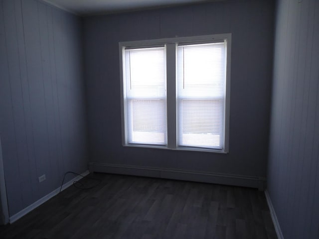 empty room featuring baseboard heating, a wealth of natural light, dark hardwood / wood-style flooring, and wood walls