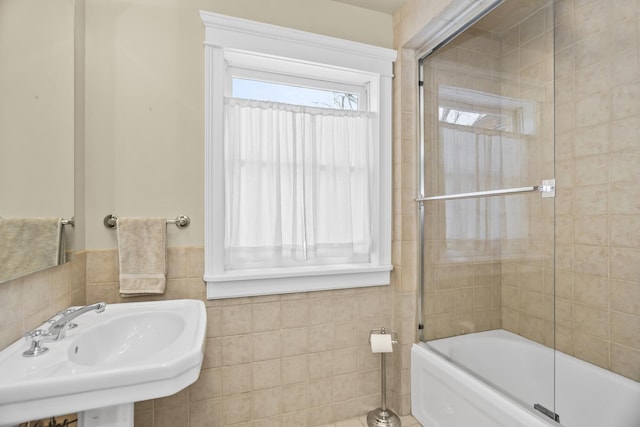 bathroom with bath / shower combo with glass door, sink, and tile walls