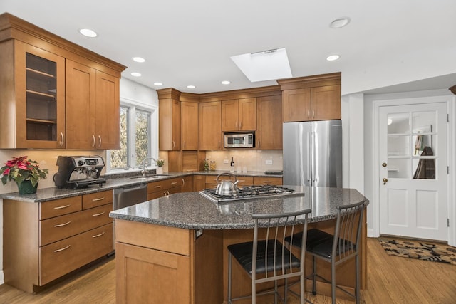 kitchen featuring a kitchen island, sink, dark stone counters, stainless steel appliances, and light wood-type flooring