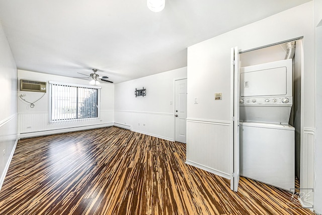 empty room with an AC wall unit, baseboard heating, dark wood-type flooring, stacked washer and dryer, and ceiling fan