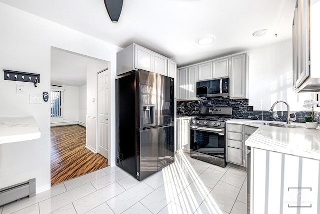 kitchen featuring a baseboard radiator, appliances with stainless steel finishes, sink, backsplash, and light stone counters