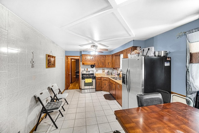 kitchen featuring appliances with stainless steel finishes, sink, tile walls, ceiling fan, and light tile patterned floors