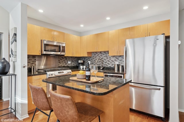 kitchen featuring stainless steel appliances, a center island, light brown cabinets, and light hardwood / wood-style flooring