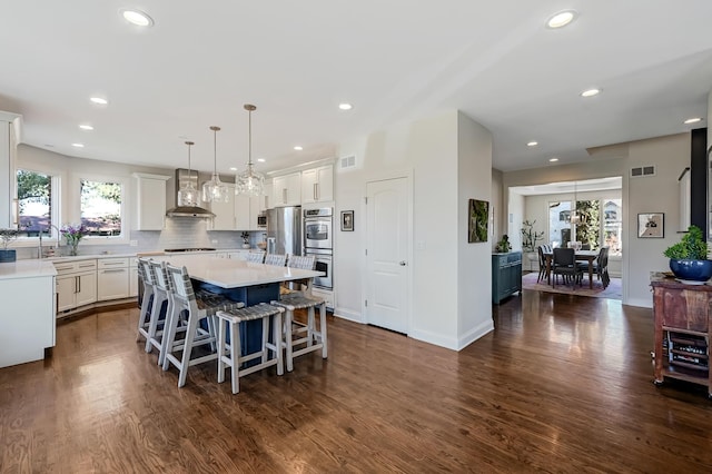 kitchen with wall chimney exhaust hood, decorative light fixtures, white cabinets, dark wood-type flooring, and a kitchen island