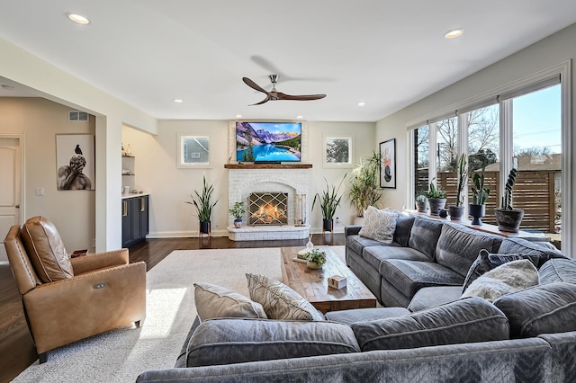 living room featuring a brick fireplace, dark wood-type flooring, and ceiling fan