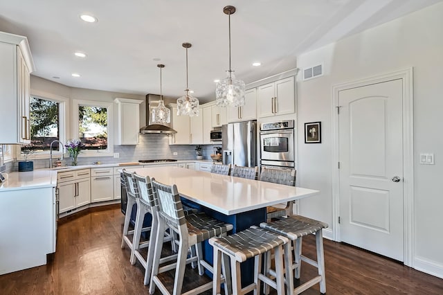 kitchen with a center island, wall chimney exhaust hood, decorative light fixtures, stainless steel appliances, and a breakfast bar area