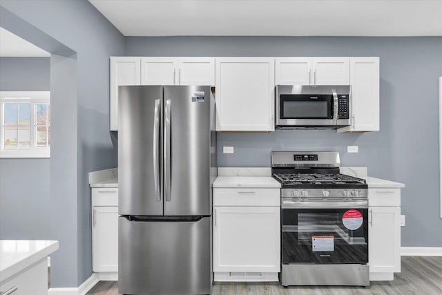 kitchen with light wood-type flooring, appliances with stainless steel finishes, and white cabinetry