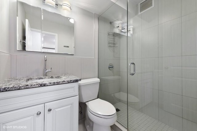 bathroom featuring tile walls, vanity, a shower with shower door, and toilet