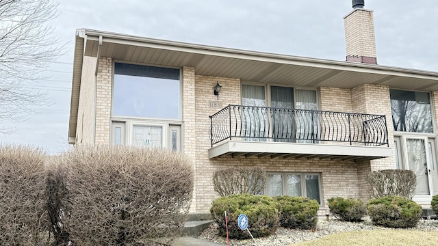 rear view of property featuring a balcony and brick siding