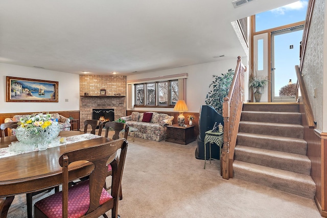 dining space with a wainscoted wall, carpet floors, visible vents, stairway, and a brick fireplace