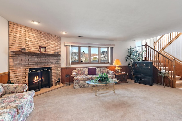 living area featuring carpet floors, wood walls, stairs, wainscoting, and a brick fireplace