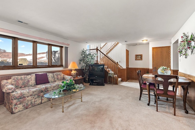 carpeted living room with a wainscoted wall, visible vents, stairway, a wood stove, and wooden walls