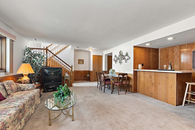 carpeted living area with stairway, wainscoting, and wooden walls