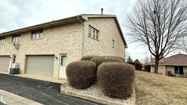 view of side of property featuring aphalt driveway, brick siding, an attached garage, and central air condition unit