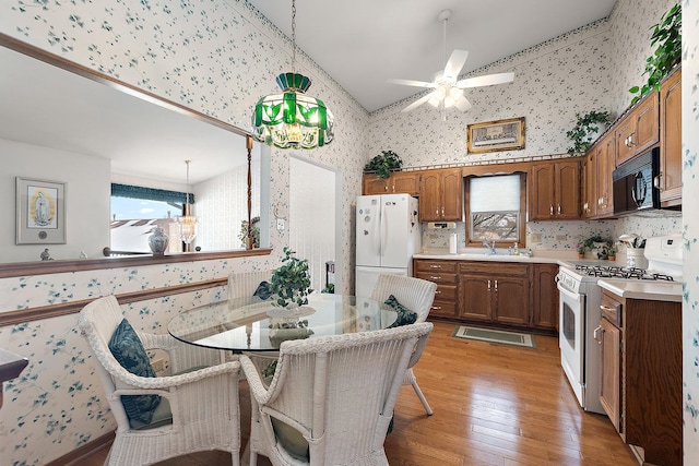 kitchen featuring light countertops, light wood-style flooring, vaulted ceiling, white appliances, and wallpapered walls