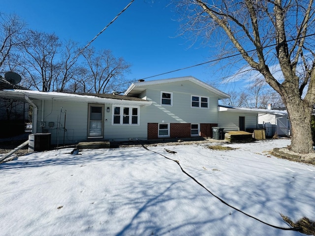 snow covered rear of property with central AC unit and a carport