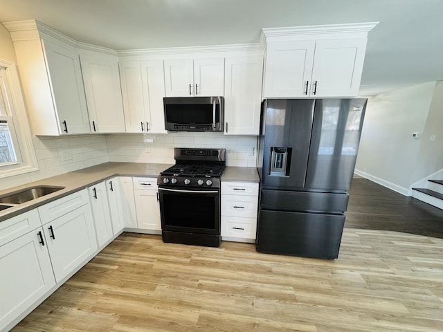 kitchen featuring light wood-type flooring, backsplash, white cabinets, and black appliances