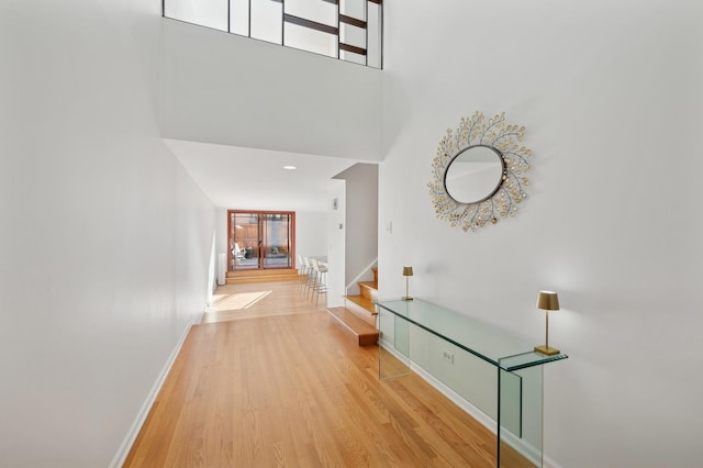 hallway featuring a towering ceiling and light wood-type flooring