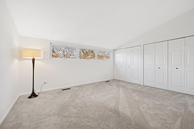 unfurnished bedroom with lofted ceiling, two closets, and carpet