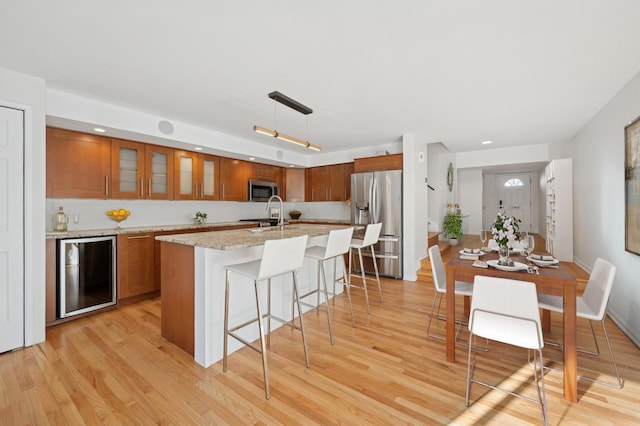 kitchen featuring wine cooler, light wood-type flooring, appliances with stainless steel finishes, an island with sink, and pendant lighting