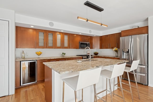 kitchen with sink, hanging light fixtures, stainless steel appliances, a center island with sink, and beverage cooler