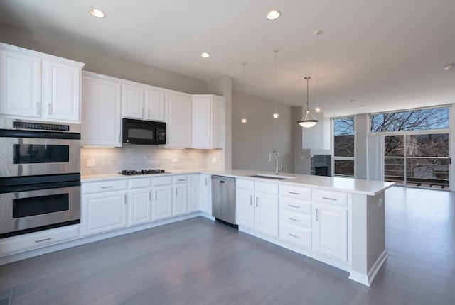 kitchen with white cabinetry, kitchen peninsula, appliances with stainless steel finishes, hanging light fixtures, and sink