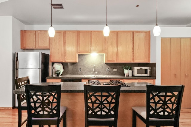 kitchen featuring a breakfast bar area, appliances with stainless steel finishes, light brown cabinets, and sink