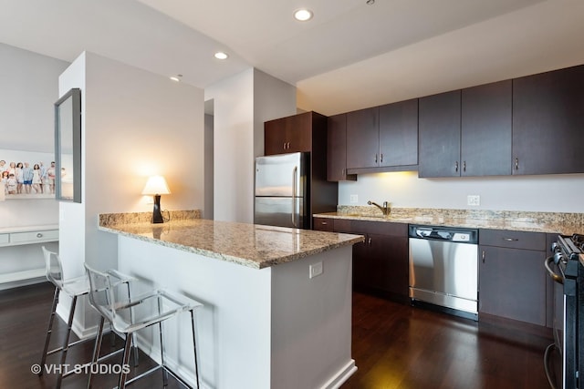 kitchen featuring appliances with stainless steel finishes, sink, dark brown cabinetry, light stone counters, and dark wood-type flooring