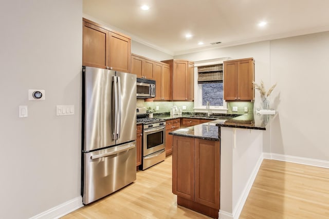 kitchen featuring appliances with stainless steel finishes, backsplash, dark stone counters, light hardwood / wood-style floors, and kitchen peninsula