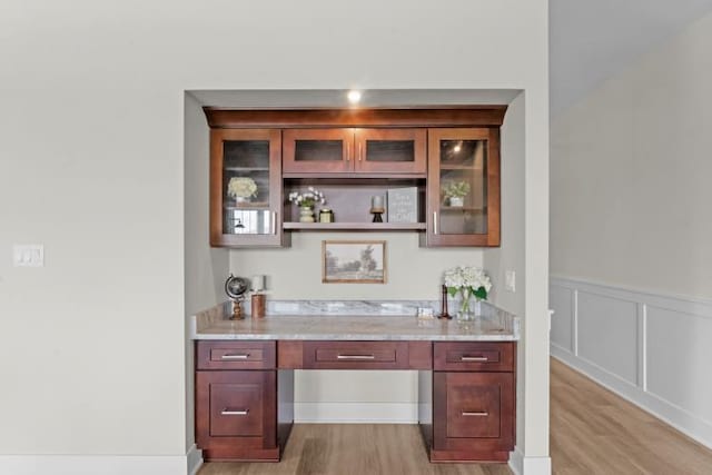 bar with built in desk, light wood-type flooring, and light stone counters