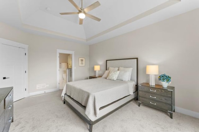 carpeted bedroom with ceiling fan, a tray ceiling, and ensuite bathroom