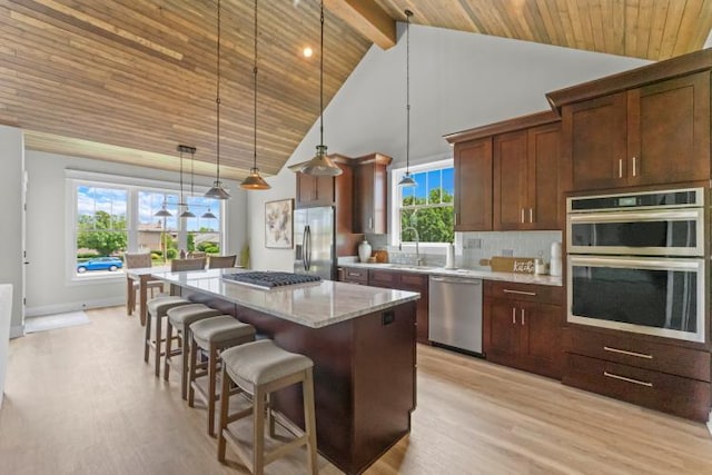 kitchen with tasteful backsplash, decorative light fixtures, a center island, appliances with stainless steel finishes, and light stone counters