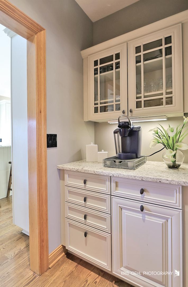 bar with light hardwood / wood-style floors, light stone countertops, and white cabinetry