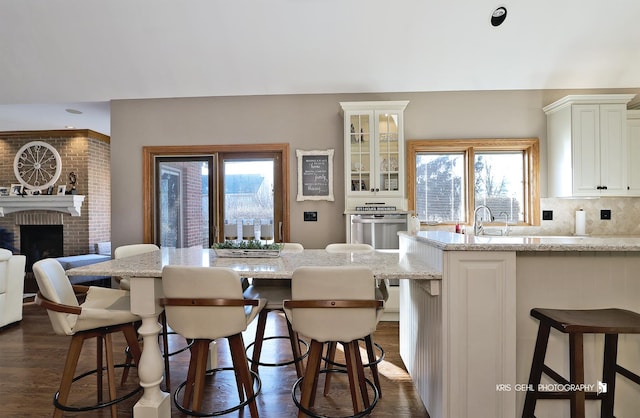 kitchen with dark wood-type flooring, a breakfast bar, light stone countertops, and a brick fireplace