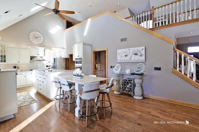 dining room with high vaulted ceiling, dark wood-type flooring, and ceiling fan