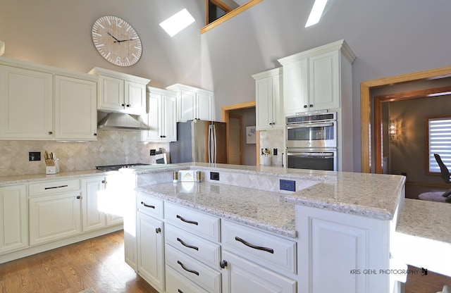 kitchen with tasteful backsplash, a high ceiling, light wood-type flooring, appliances with stainless steel finishes, and light stone counters