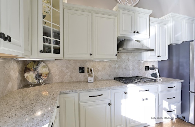 kitchen with stainless steel appliances, wall chimney exhaust hood, white cabinets, and tasteful backsplash