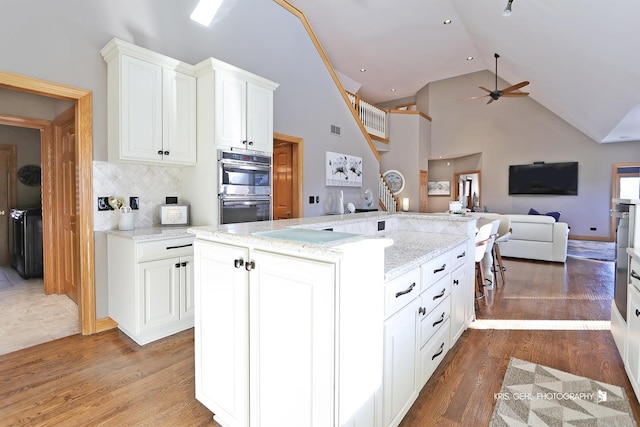 kitchen featuring white cabinetry, hardwood / wood-style floors, tasteful backsplash, light stone countertops, and double oven