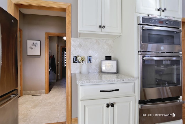 kitchen featuring decorative backsplash, light stone counters, stainless steel appliances, and white cabinetry