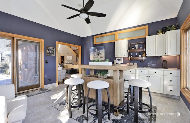 kitchen featuring ceiling fan, white cabinets, a kitchen bar, and vaulted ceiling