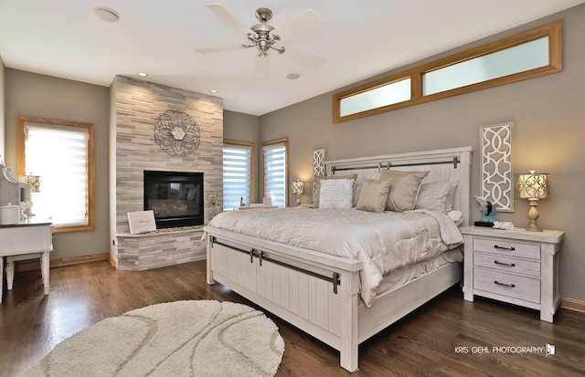 bedroom featuring dark wood-type flooring, ceiling fan, a fireplace, and multiple windows