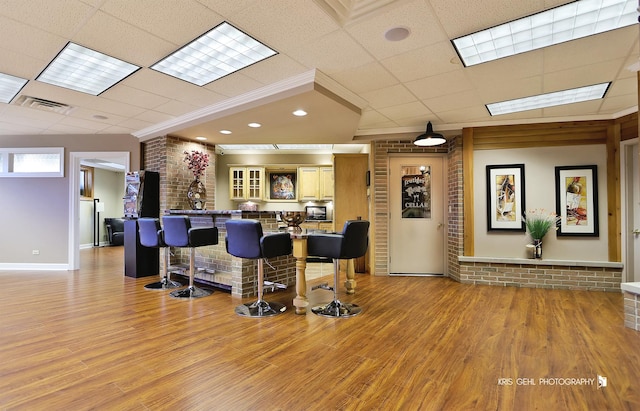 bar featuring a paneled ceiling, brick wall, ornamental molding, and light hardwood / wood-style floors