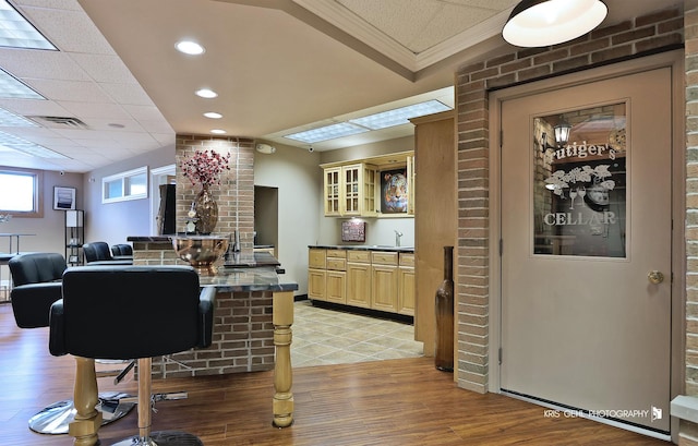 bar with light hardwood / wood-style floors, brick wall, ornamental molding, cream cabinets, and sink