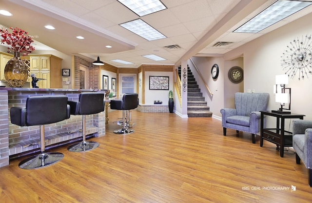 bar with a paneled ceiling, ornamental molding, and light hardwood / wood-style flooring