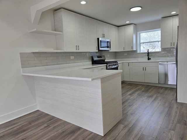 kitchen with tasteful backsplash, wood-type flooring, white cabinets, kitchen peninsula, and stainless steel appliances