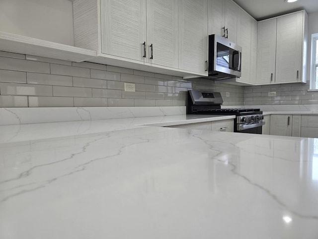 kitchen featuring stainless steel appliances, backsplash, and light stone counters